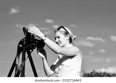 A woman photographer adjusts the camera for shooting. Black and white photo of a beautiful blonde girl with a camera - Powered by Shutterstock