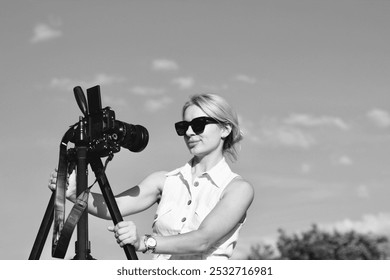 A woman photographer adjusts the camera for shooting. Black and white photo of a beautiful blonde girl with a camera - Powered by Shutterstock