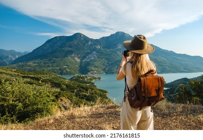 Woman photographer with big backpack taking photo of mountains and blue lake. Travel and hobby concept - Shutterstock ID 2176161815