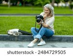 A woman photographer with a camera in her hands sits in a summer park and looks at the pictures. She is overwhelmed with emotion when she sees the results of her work