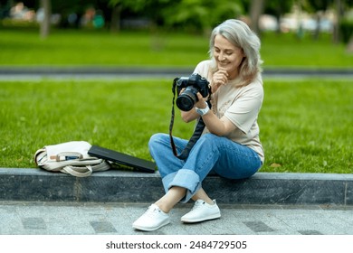 A woman photographer with a camera in her hands sits in a summer park and looks at the pictures. She is overwhelmed with emotion when she sees the results of her work - Powered by Shutterstock