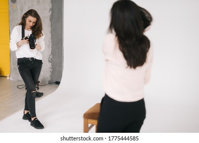 Woman photographer and female model together looking at made photo and talking,smiling, white background. Concept of creative work in photo studio, backstage job.