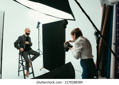 Woman photographer makes a photo shoot for a positive bearded man in a photo studio on a white background. Backstage - Shutterstock ID 2170288389