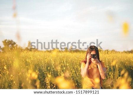Woman photographer with mirrorless camera on the yellow  flower meadow 