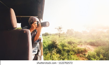 Woman photographer takes a picture with professional camera from touristic vehicle on tropical safari