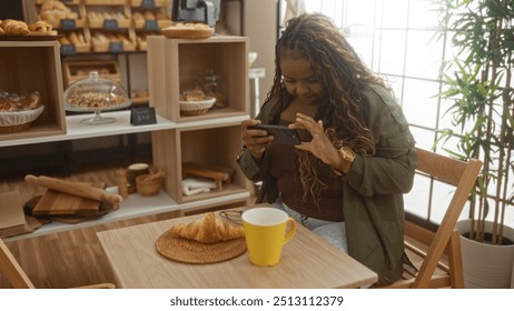 Woman photographing a croissant and coffee on a table in a cozy bakery shop with shelves of bread in the background - Powered by Shutterstock