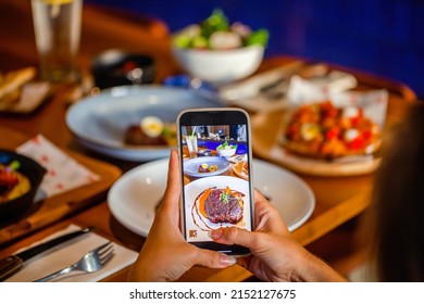 Woman Photographing Gourmet Steak Through Mobile Phone At Luxury Restaurant Table. Hand Hold Smartphone And Taking Photo Of Meat On Dish Before Eating In Cafe.