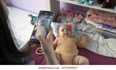 Woman photographing her baby with a smartphone, infant girl lying on changing table, selective focus - Shutterstock ID 2272569027