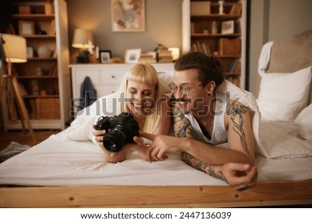 Woman photographing her tattooed husband with a camera in bed