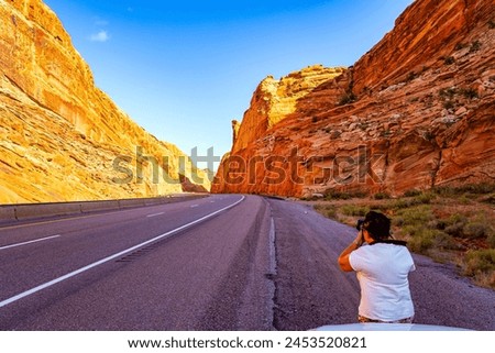 Woman photographing magnificent landscape. The smooth asphalt highway runs between the picturesque ridges of the San Rafael Reef