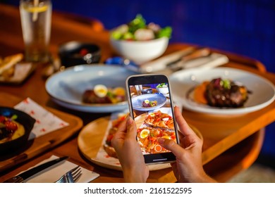 Woman Photographing Salmon Toast Through Mobile Phone At Table In Restaurant. Hands Hold Smartphone Taking Photo Of Fine Dining Food In Cafe. Smartphone Food Photography Of Lunch Or Dinner