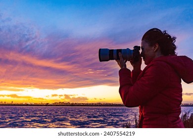 Woman photographing seascape at sunset with professional camera.