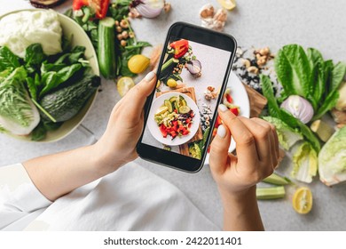 A woman photographs a fresh vegetable salad on the kitchen table. - Powered by Shutterstock