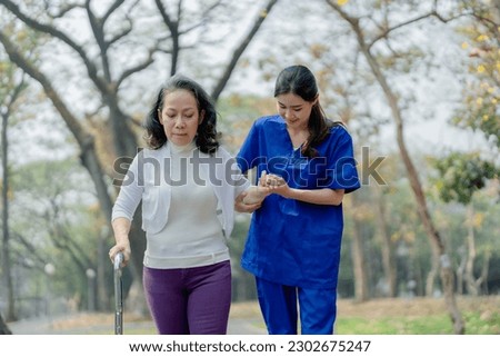 woman physiotherapist is holding a female elderly patient walking in a park to strengthen her leg muscles