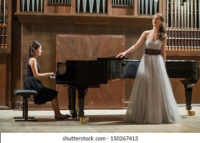 Woman pianist plays the piano and beautiful singer stands next