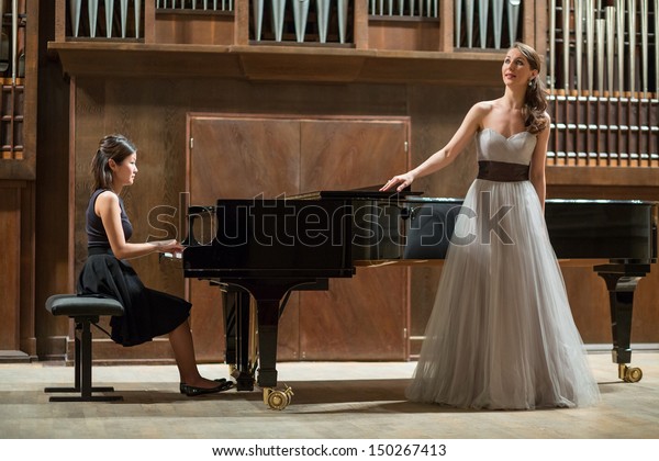 Woman pianist plays the piano and beautiful singer\
stands next