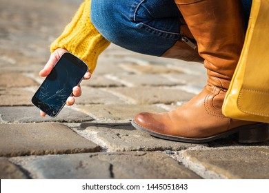 Woman picking up damaged smartphone with cracked touch screen on the street. Broken mobile phone. 