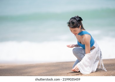 Woman Picking Up Shells And Holding Them In Hand On The Beach.