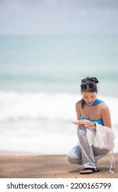 Woman Picking Up Shells And Holding Them In Hand On The Beach.