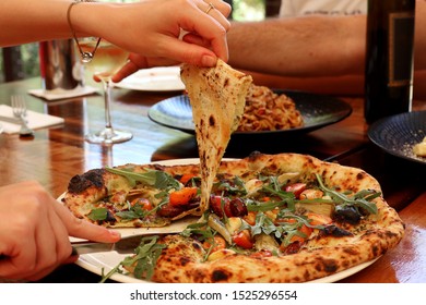 Woman Picking Up Slice Of Marinated Artichoke Pizza 