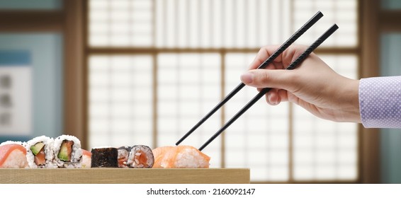 Woman Picking Up Sushi Using Chopsticks, She Is Having Lunch At The Japanese Restaurant