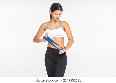 Woman Pilates Trainer Stands Against A White Wall With An Elastic Band For Training