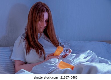 Woman with pills in bed at home. Night exposure. Lady with long brown hair wearing a nightgown. Girl lying in a nightie on clean white bed linen with cozy blanket.