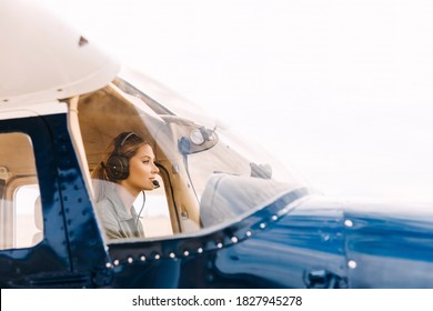 Woman pilot in airplane cockpit, wearing headset with microphone.