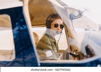 Woman pilot in airplane cockpit, wearing headset and sunglasses.
