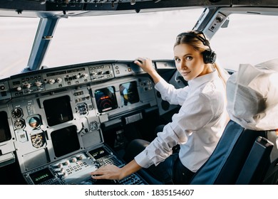 Woman pilot flying a commercial airplane, wearing headset, looking at camera, smiling.