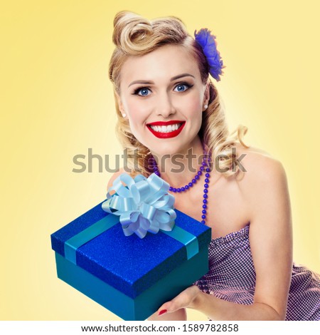 Woman in pin up style blue dress, over yellow background. Caucasian blond girl - retro fashion. Sales and holiday gift concept. Square composition.