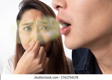 A woman pinching her nose due to bad breath in a man.