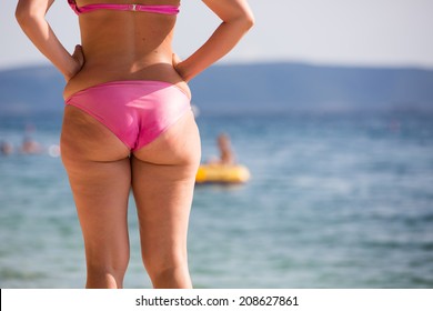 Woman in pink bikini at a beach, watching the sea, hesitating before going for a swim