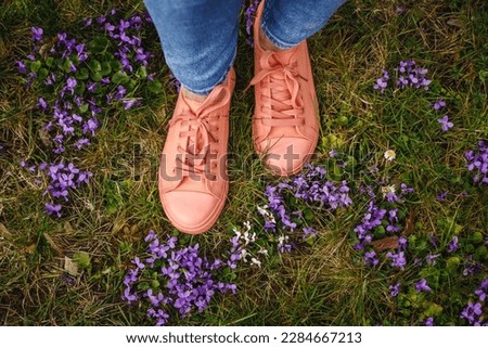 Woman with pink canvas shoes standing in meadow with violet flowers. Spring fashion season