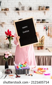 Woman In Pink Dress Holding Black Letter Board With Words Happy Easter, Standing In The Kitchen