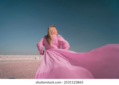 Woman Pink Dress Wind Salt Flats Pose. A woman in a pink dress twirls with her arms above her head, the fabric billowing in the wind. The background is a vast, white, sandy expanse under a blue sky. - Powered by Shutterstock