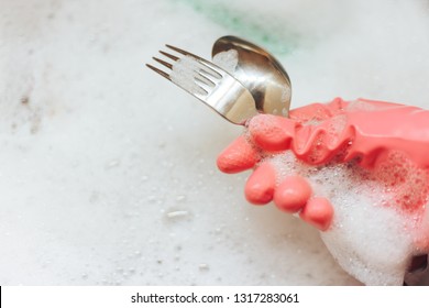 A woman in a pink glove washes dishes with a green sponge. Fork and knife Shine after cleaning. A lot of foam in the washstand. - Powered by Shutterstock