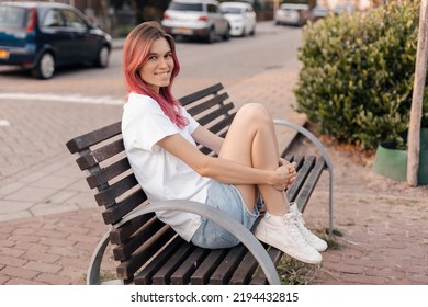 Woman with pink hair sitting on bench and smiling, walking in park, looking carefree and happy. Modern girl breathing fresh air on a walk, look free and joyful. - Powered by Shutterstock