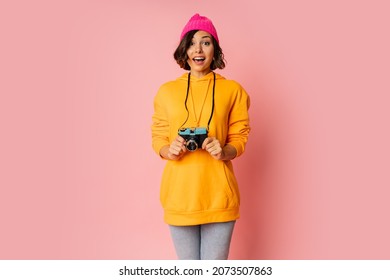 Woman In Pink Hat And  Orange Hoodie  With  Suprice Face  Using Photo Camera On Pink Bacground. 