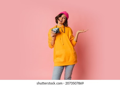 Woman In Pink Hat And  Orange Hoodie  With  Suprice Face  Using Photo Camera On Pink Bacground. 