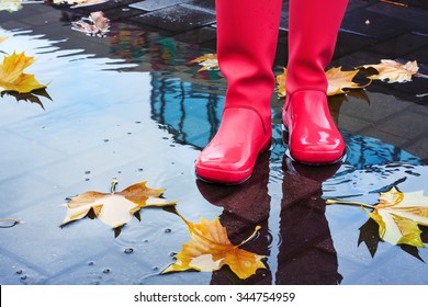 Woman with pink rain boots jumps into a puddle on rainy autumn day
