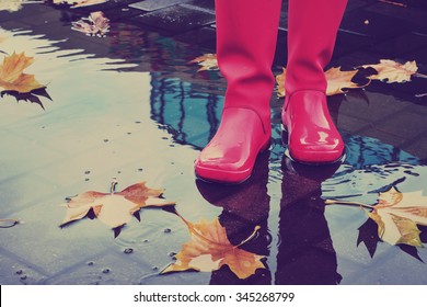 Woman With Pink Rain Boots Jumps Into A Puddle On Rainy Autumn Day. Toned Image