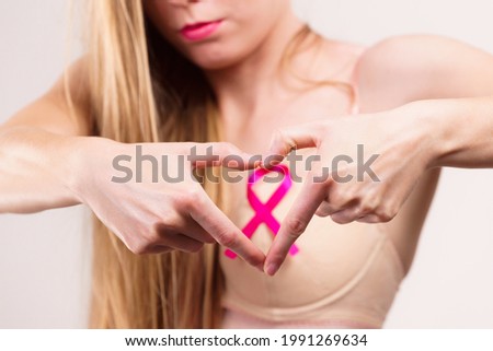 Woman pink ribbon on chest making heart shape with her hands. Breast cancer awareness.