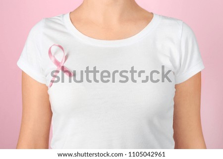 Woman with pink ribbon on t-shirt against color background. Breast cancer awareness concept