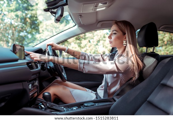 woman in pink suit in car, behind\
right wheel of car, selects application on touch screen display,\
selects route, in summer in city, business lady goes to\
meeting