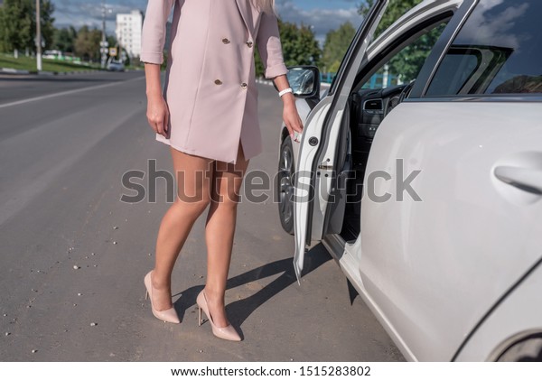 A woman in a pink suit opens car door, in the\
summer in the city, business taxi, tanned skin, long legs,\
high-heeled shoes.