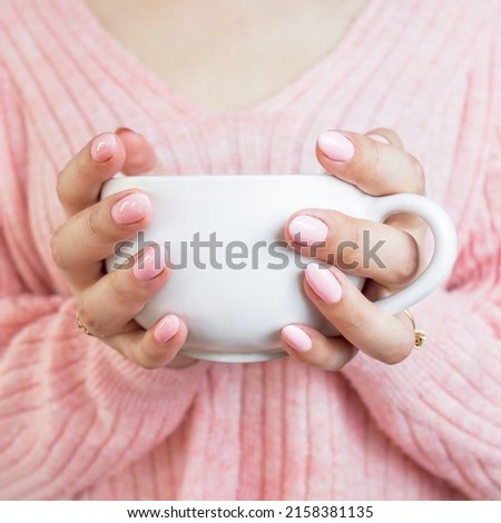 woman in a pink sweater with a pink manicure holds a large cup with hot coffee or tea, close-up. pink 