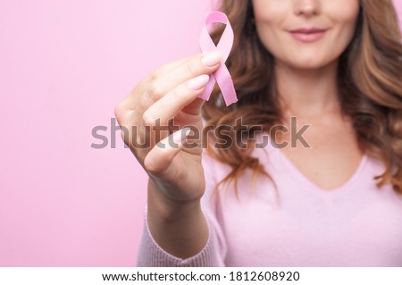 Woman in pink sweater with pink ribbon supporting breast cancer awareness campaign. Breast Cancer Awareness Month