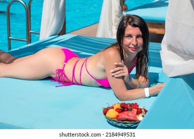 A Woman In A Pink Swimsuit Is Sunbathing On A Beach Lounger With A Fruit Plate And A Drink. Tourism And Recreation