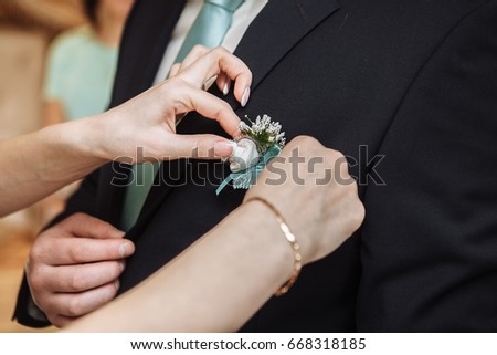 Woman pinning the boutonniere on the groom's jacket. Close up picture. Unrecognizable man. Horizontal format